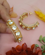 Load image into Gallery viewer, Close-up of a handcrafted gold-plated Kundan Jadau bangle featuring large oval stones and shimmering CZ diamond borders on a pink background with floral accents.