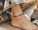 Load image into Gallery viewer, Close-up of a 2005-born Rajasthani Gen Z model wearing a handcrafted oxidized silver anklet with black crystal beads, engraved silver spacers, adjustable chain, and a blue evil eye charm, styled with a contemporary ethnic outfit in natural sunlight.