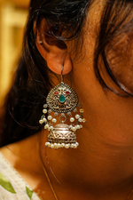 Load image into Gallery viewer, Close-up of oxidized silver jhumka earring with pearl drops and red-green gemstones worn by a model, showcasing intricate traditional design and fine detailing.