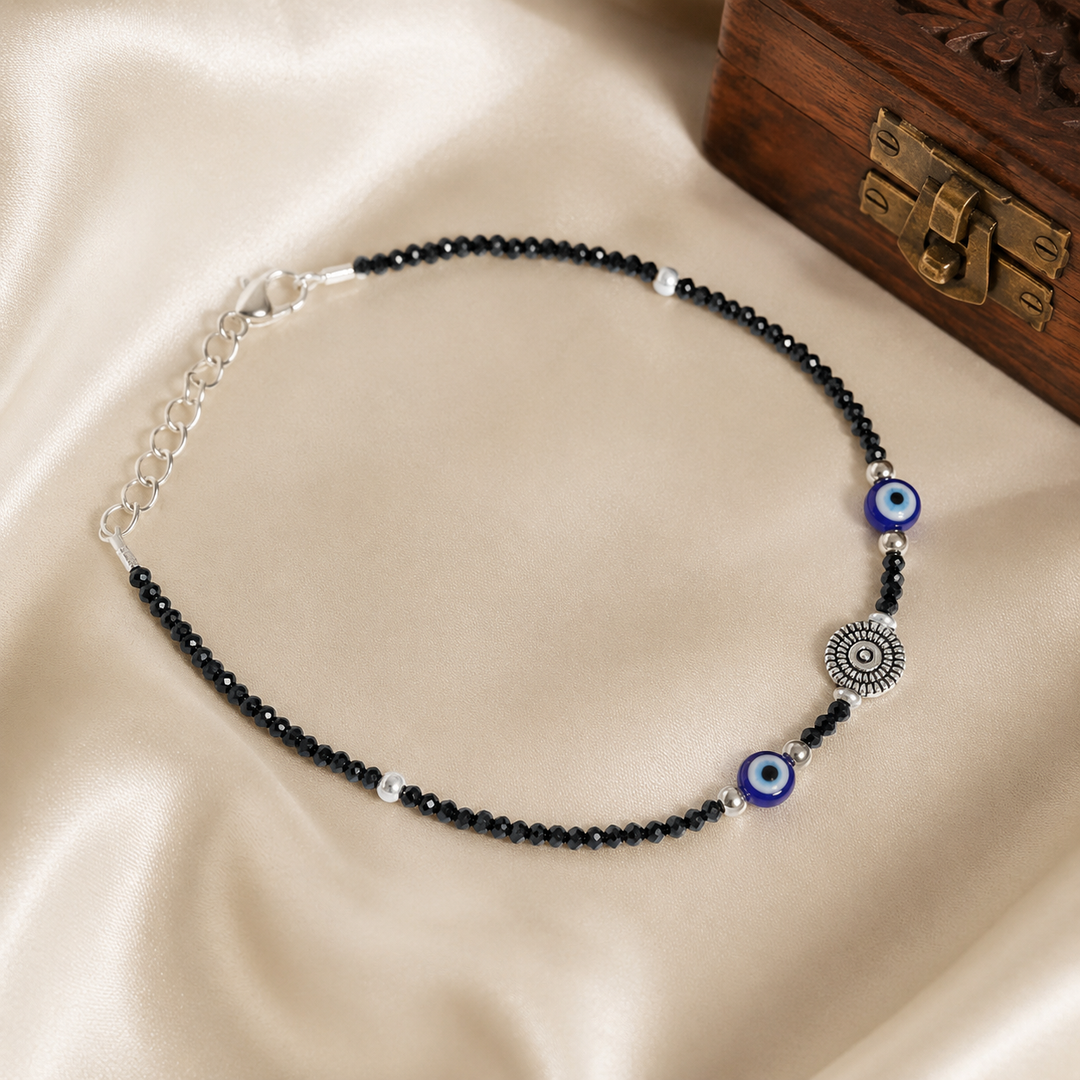 Black crystal evil eye oxidized silver anklet for women with adjustable chain on a soft satin background.