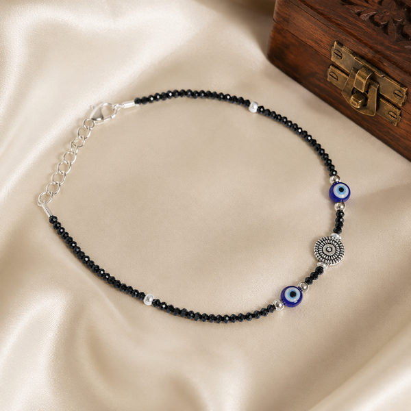 Black crystal evil eye oxidized silver anklet for women with adjustable chain on a soft satin background.