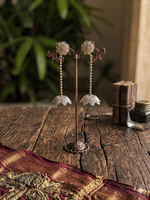 Load image into Gallery viewer, A pair of intricate handcrafted silver dangle earrings on a stylized dark wooden display stand, showcasing beaded chains and floral accents.
