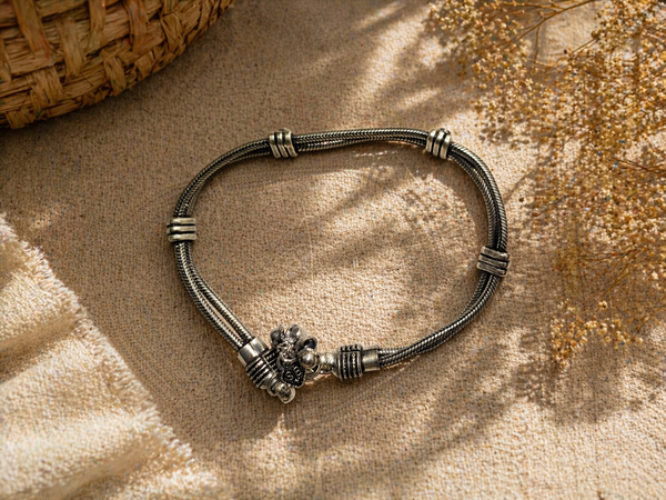 Oxidized silver anklet worn on a foot in natural sunlight, styled on a woven mat with soft fabric and dried flowers for a candid boho aesthetic.