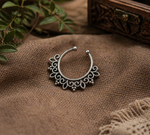 Load image into Gallery viewer, Oxidized silver septum ring with intricate filigree detailing placed on textured brown fabric with wooden elements and greenery in a warm rustic setting.
