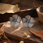 Load image into Gallery viewer, oxidized silver flower stud earrings with textured petals placed on rustic wooden surface with dried leaves and warm natural lighting
