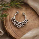 Load image into Gallery viewer, Oxidized silver septum ring with intricate scroll detailing placed on a wooden surface with soft fabric and greenery, styled in natural light for a rustic aesthetic.
